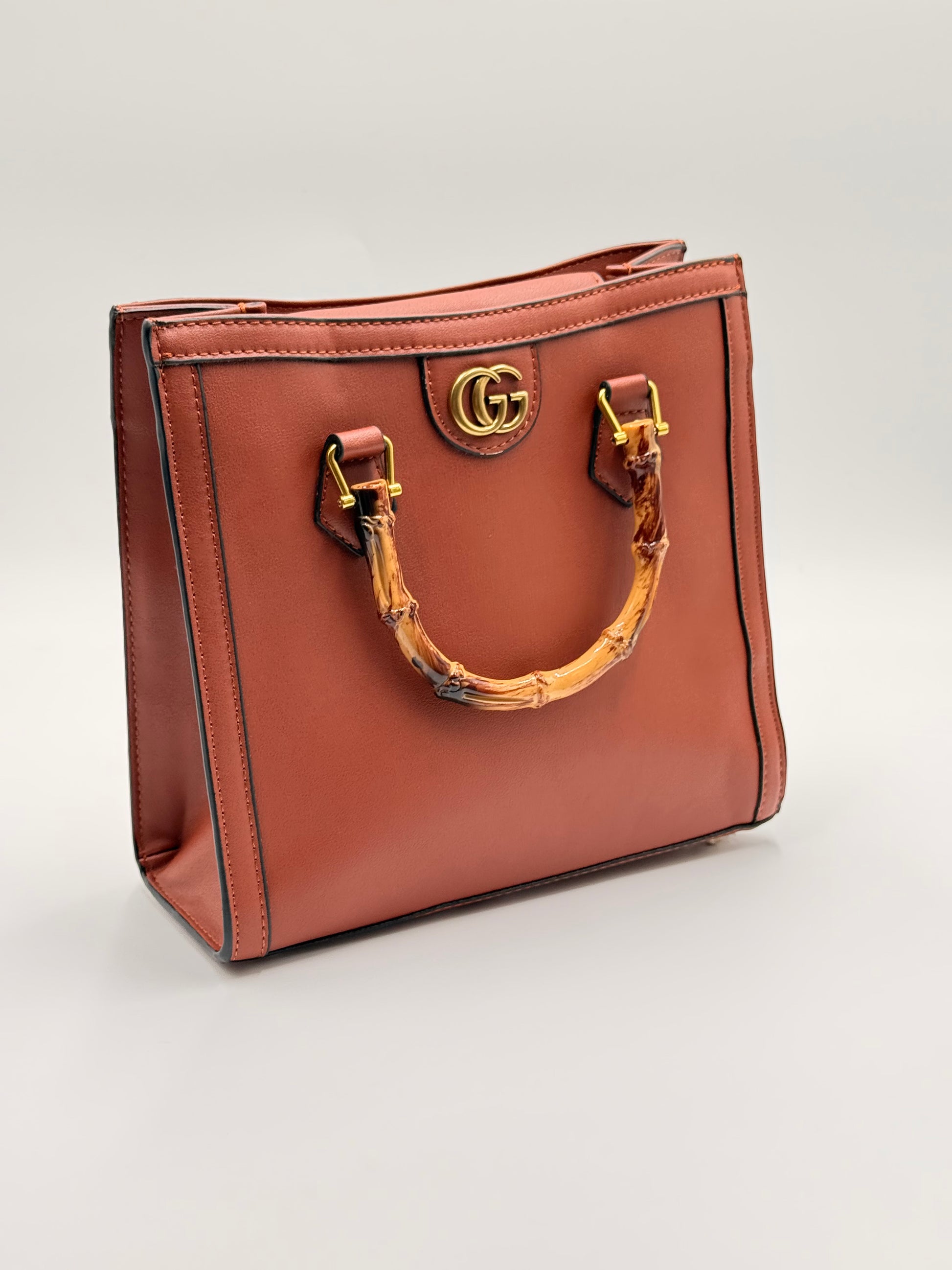 Brown leather handbag with gold hardware on a light gray background