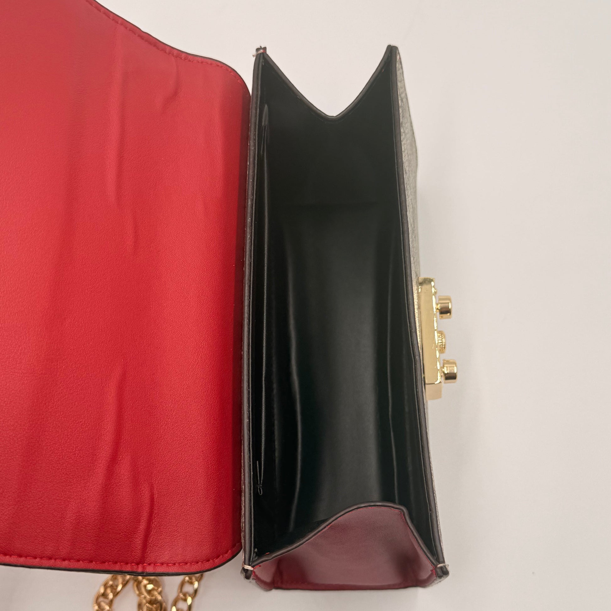 Black handbag with gold chain on a red surface