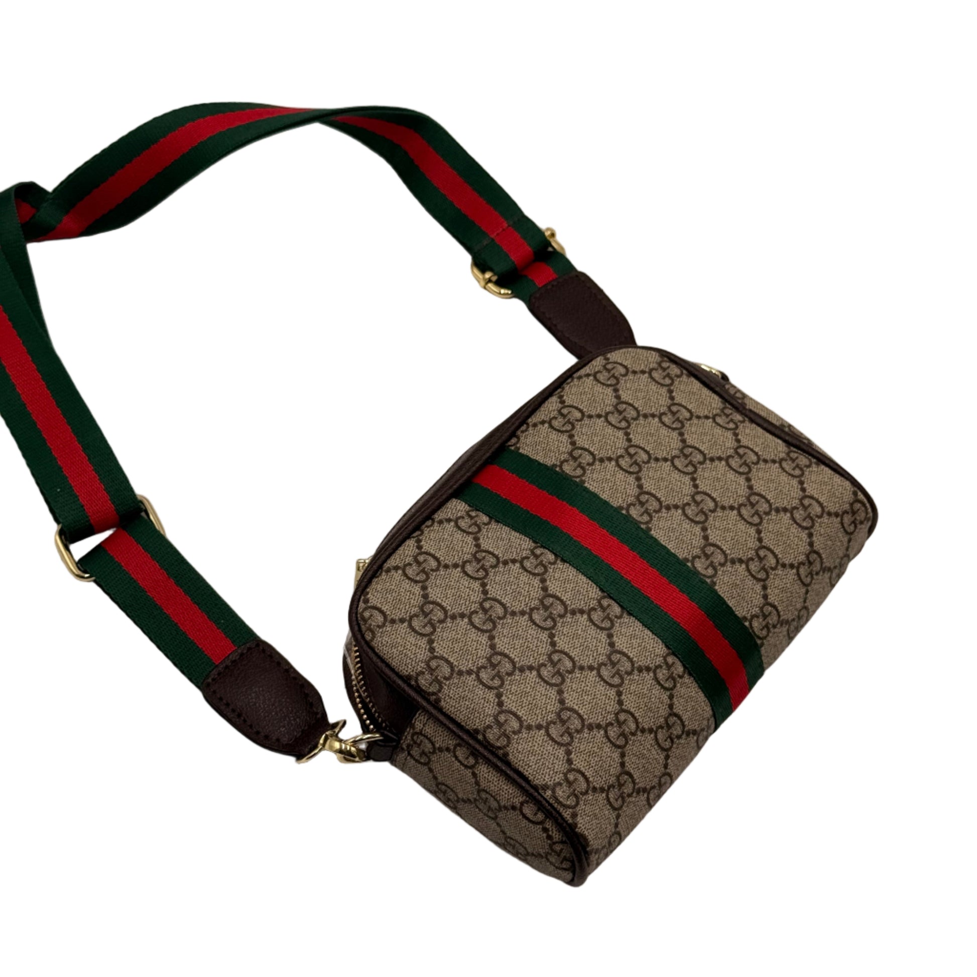 Designer bag with patterned surface and red and green strap on a light gray background
